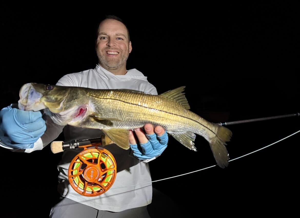 Angler holding a snook caught at night with a fly rod, a striking example of what is fly fishing for coastal species in low-light conditions.